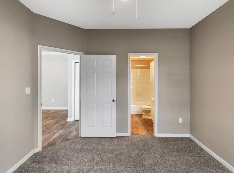 Bedroom with tan walls, white trim, en suite bathroom, and wall to wall carpet